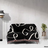 Black and white scribble lined woven blanket throw with fringe draped over a couch against a white wall.