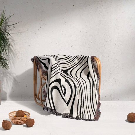 Simple black and white modern couch woven throw blanket draped over a chair with a minimal background