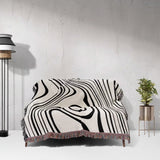 Simple black and white modern couch woven throw blanket on a couch against a white wall with a lamp and plant in the background.