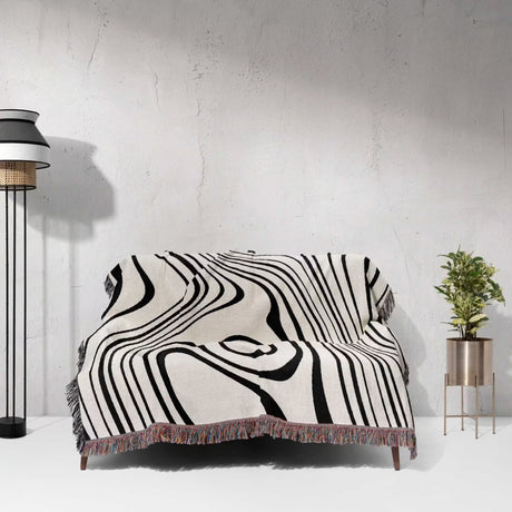 Simple black and white modern couch woven throw blanket on a couch against a white wall with a lamp and plant in the background.