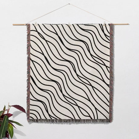 Black and white simple curly lines woven blanket throw with wavy pattern hanged on a white wall.