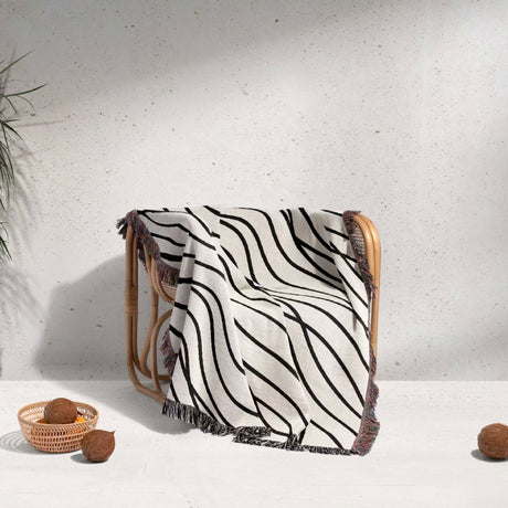 Black and white simple curly lines woven blanket throw draped over a chair against a white wall with decorative elements.