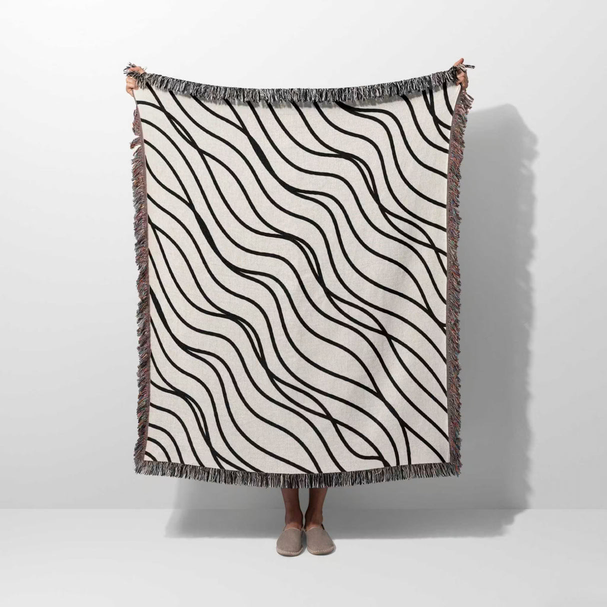 Person holding a black and white simple curly lines woven blanket throw against a white background.
