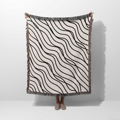 Person holding a black and white simple curly lines woven blanket throw against a white background.