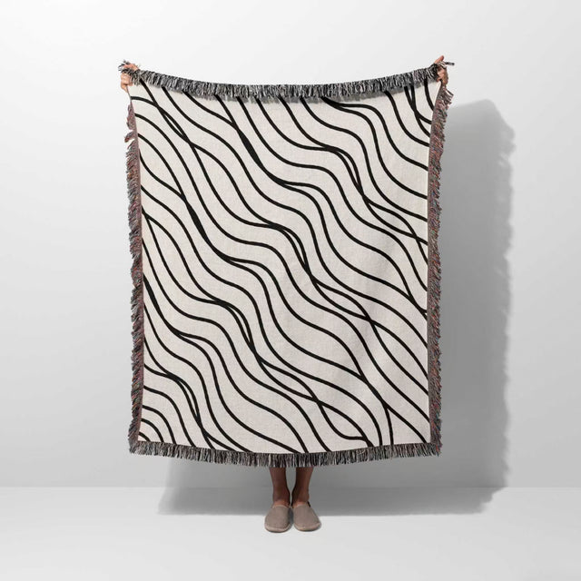 Person holding a black and white simple curly lines woven blanket throw against a white background.