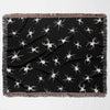 A horizontally laid out Halloween-themed woven blanket. The blanket displays a pattern of white spiders on a dark, black background. The multicolor fringe adds a decorative border to the blanket.