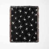 A vertically arranged Halloween woven blanket showcasing white spider designs on a deep black background. The blanket’s multicolor fringe stands out against the dark theme, adding a vibrant touch.