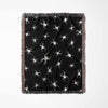 A vertically arranged Halloween woven blanket showcasing white spider designs on a deep black background. The blanket’s multicolor fringe stands out against the dark theme, adding a vibrant touch.