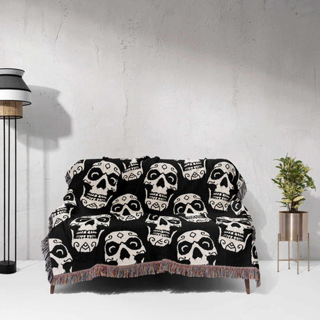 Black blanket with white skull patterns draped over a sofa against a light gray wall.