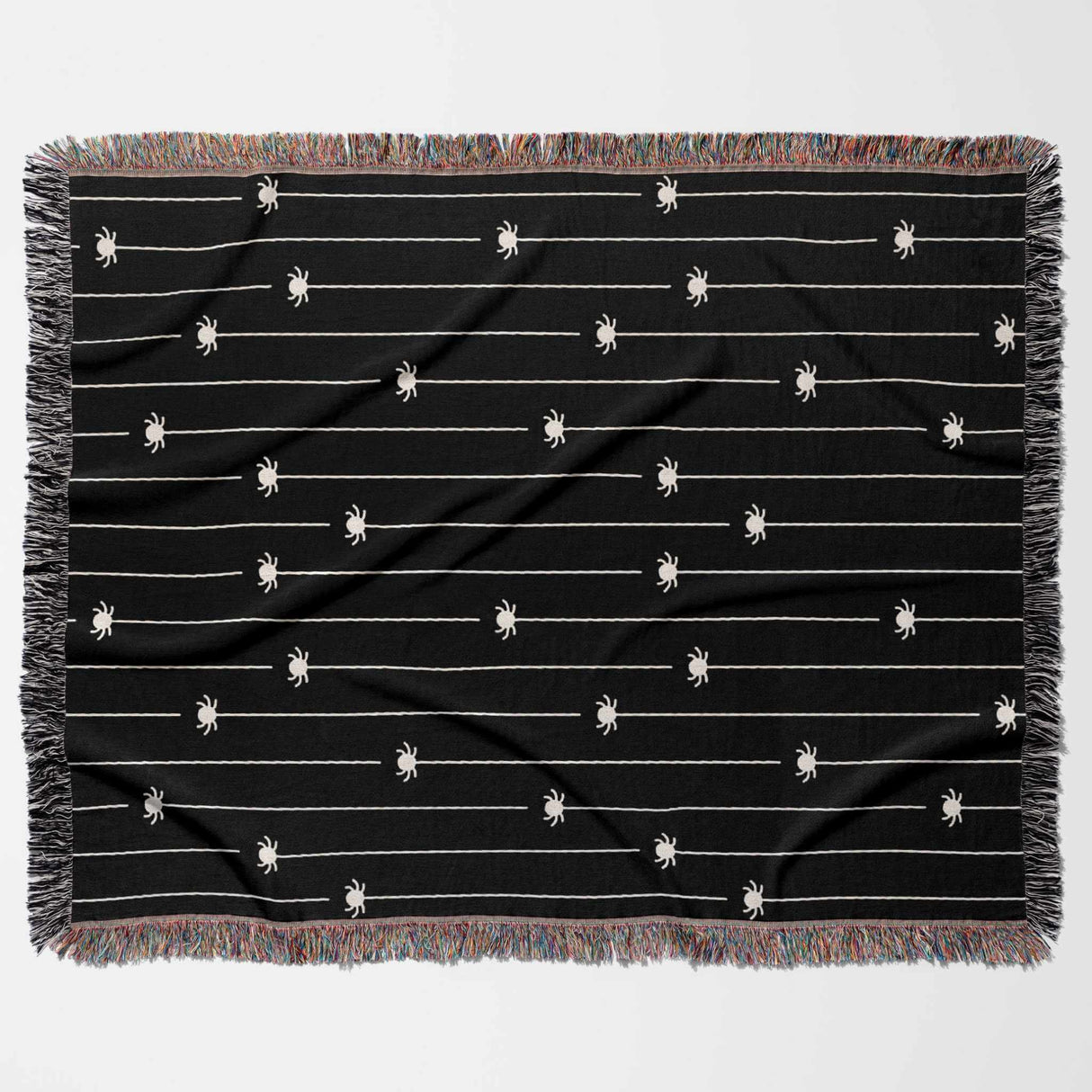 This flat-lay image displays the entire Spooky Halloween Woven Blanket in a horizontal position. The design features multiple off-white spiders hanging from thin lines on a solid black background. The blanket’s multicolored fringe adds a playful touch to the eerie spider pattern, making it a perfect Halloween-themed throw for any space.