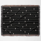 This flat-lay image displays the entire Spooky Halloween Woven Blanket in a horizontal position. The design features multiple off-white spiders hanging from thin lines on a solid black background. The blanket’s multicolored fringe adds a playful touch to the eerie spider pattern, making it a perfect Halloween-themed throw for any space.