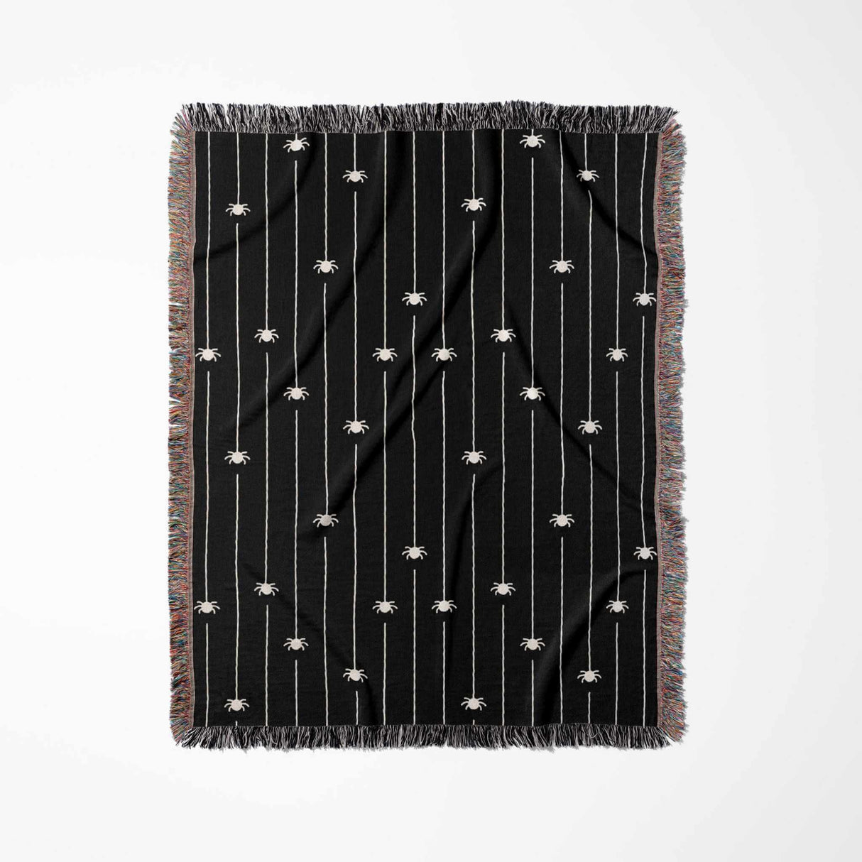 This image showcases the Spooky Halloween Woven Blanket in a vertical flat-lay view. The design consists of numerous off-white spiders suspended from threads on a deep black background, creating a striking contrast. The blanket is bordered with a multicolored fringe, which complements the black and white theme while adding a splash of color.