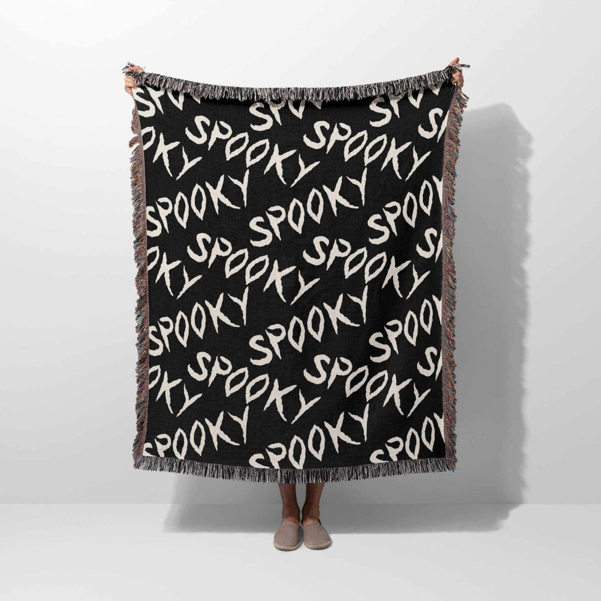 Black blanket with 'spooky' text pattern draped over a person on a white background