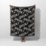 Black blanket with 'spooky' text pattern draped over a person on a white background
