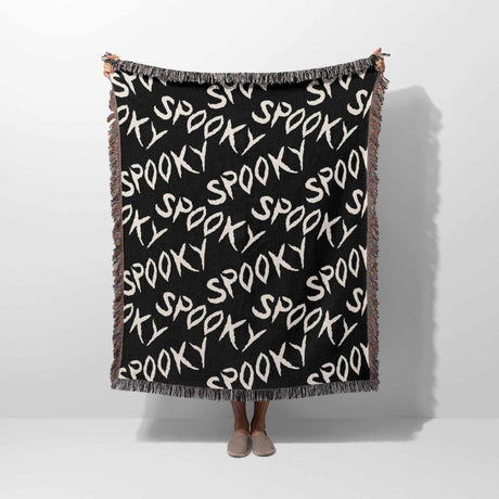 Black blanket with 'spooky' text pattern draped over a person on a white background