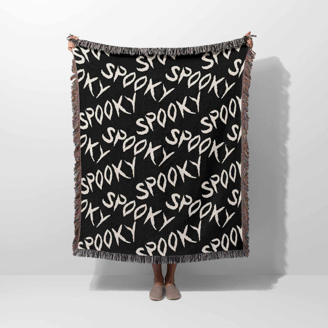 Black blanket with 'spooky' text pattern draped over a person on a white background