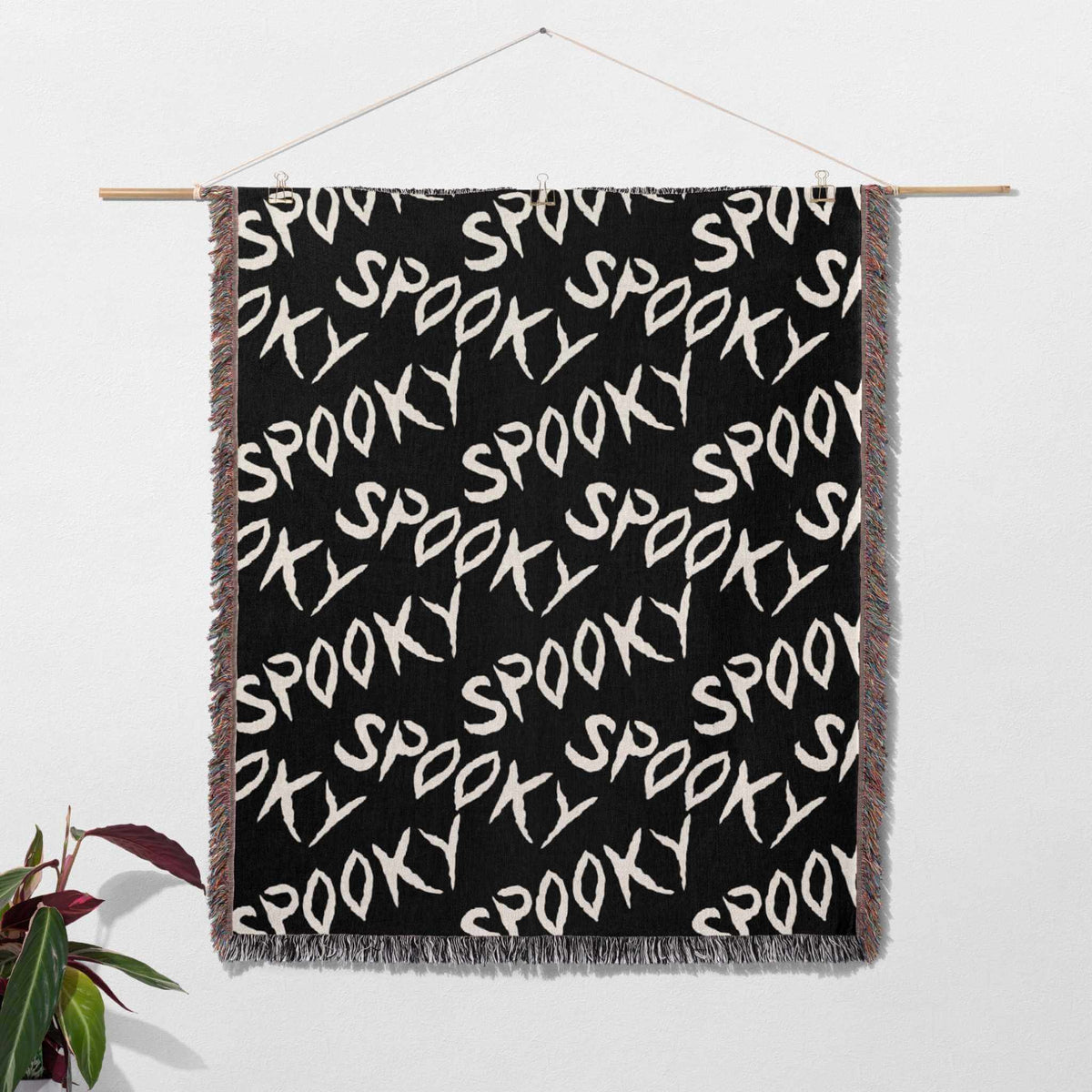 Black blanket with 'SPOOKY' text pattern hanging on a white wall.