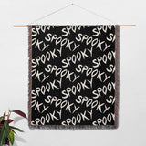 Black blanket with 'SPOOKY' text pattern hanging on a white wall.
