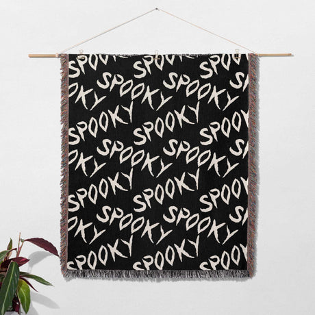 Black blanket with 'SPOOKY' text pattern hanging on a white wall.