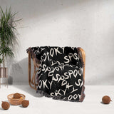 Black blanket with white text draped over a chair against a light gray wall.
