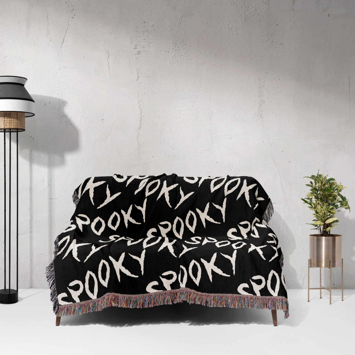 Black blanket with 'Spooky' pattern draped over a chair against a white wall.