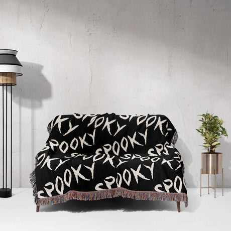 Black blanket with 'Spooky' pattern draped over a chair against a white wall.