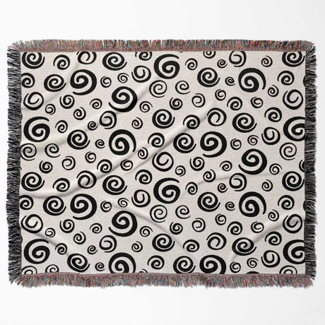 Black and white swirls patterned woven blanket throw with fringe horizontally flat lay on a white background.