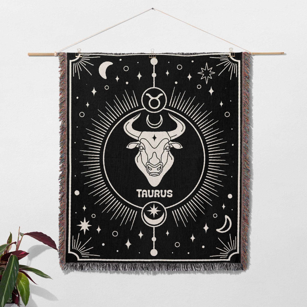 Taurus Zodiac Blanket used as wall art decor. The black and white woven throw blanket with the Taurus symbol and celestial patterns is hung on a wall, showcasing its artistic design and versatility.