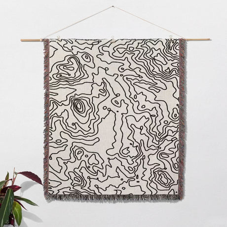 Black and white topographic map design woven throw blanket as woven wall art with black line pattern on a white background.