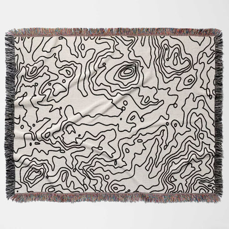 Black and white topographic map design woven throw blanket with black line art pattern flat lay on a light background.