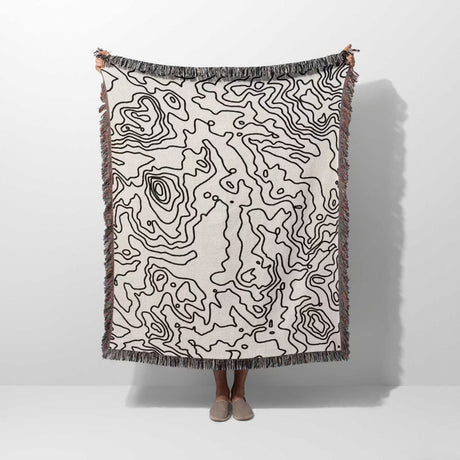 Person holding a black and white topographic map design woven throw blanket on a white background.