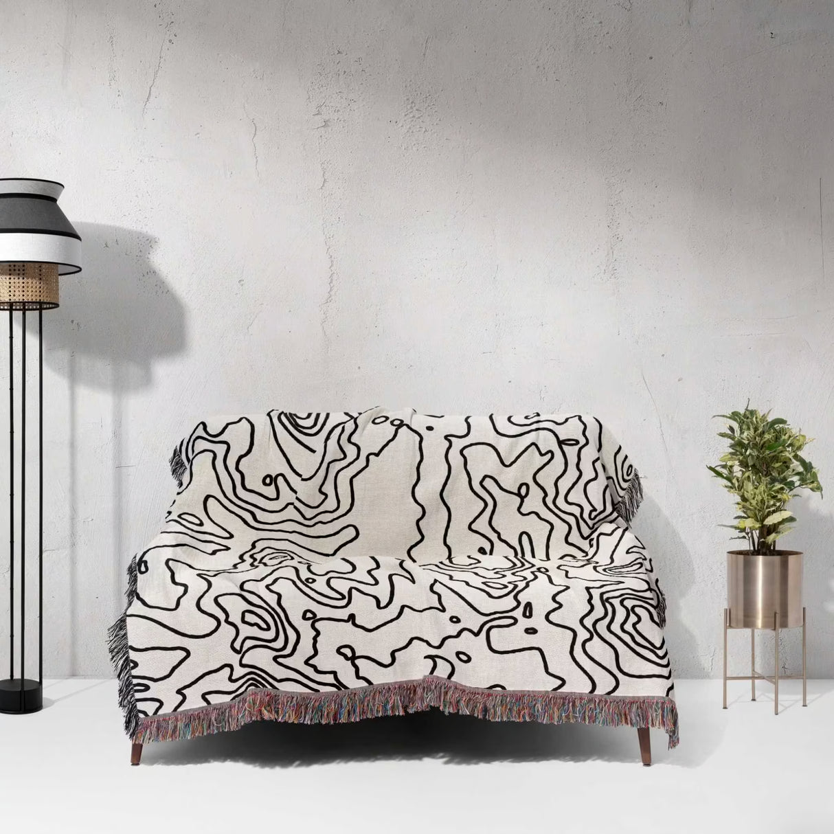 Sofa with a black and white topographic map design woven throw blanket against a white wall.