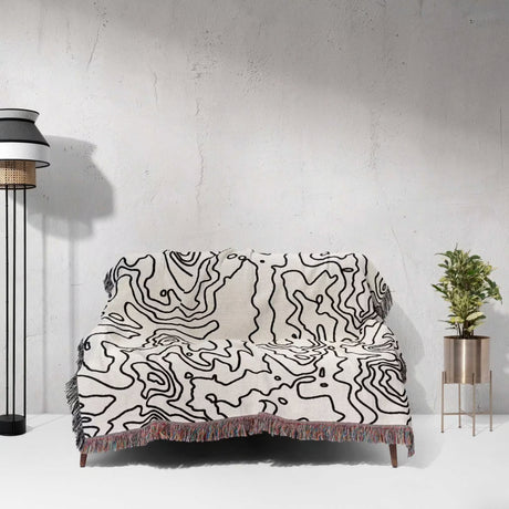 Sofa with a black and white topographic map design woven throw blanket against a white wall.