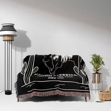 Two horses 2nd anniversary gift woven throw blanket with white horse design draped over a couch in a room with a lamp and plant.