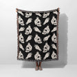 Black blanket with white skull and bottle pattern draped over a person on a white background