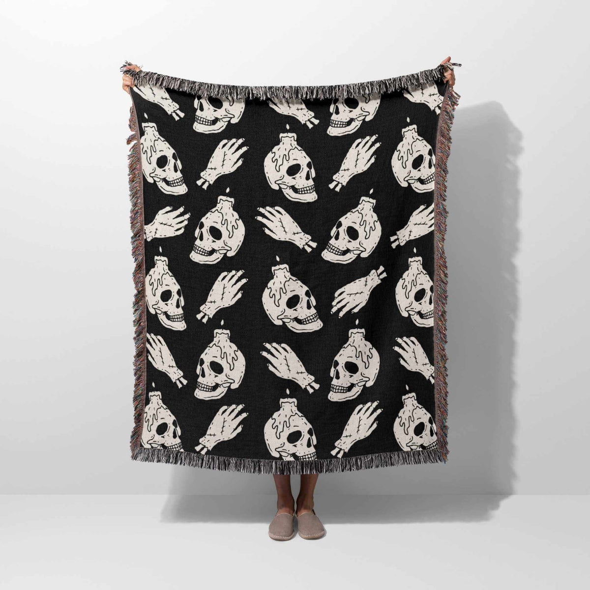 Black blanket with white skull and bottle pattern draped over a person on a white background