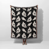 Black blanket with white skull and bottle pattern draped over a person on a white background