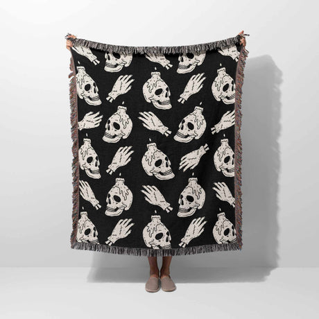 Black blanket with white skull and bottle pattern draped over a person on a white background
