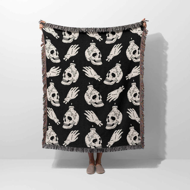 Black blanket with white skull and bottle pattern draped over a person on a white background