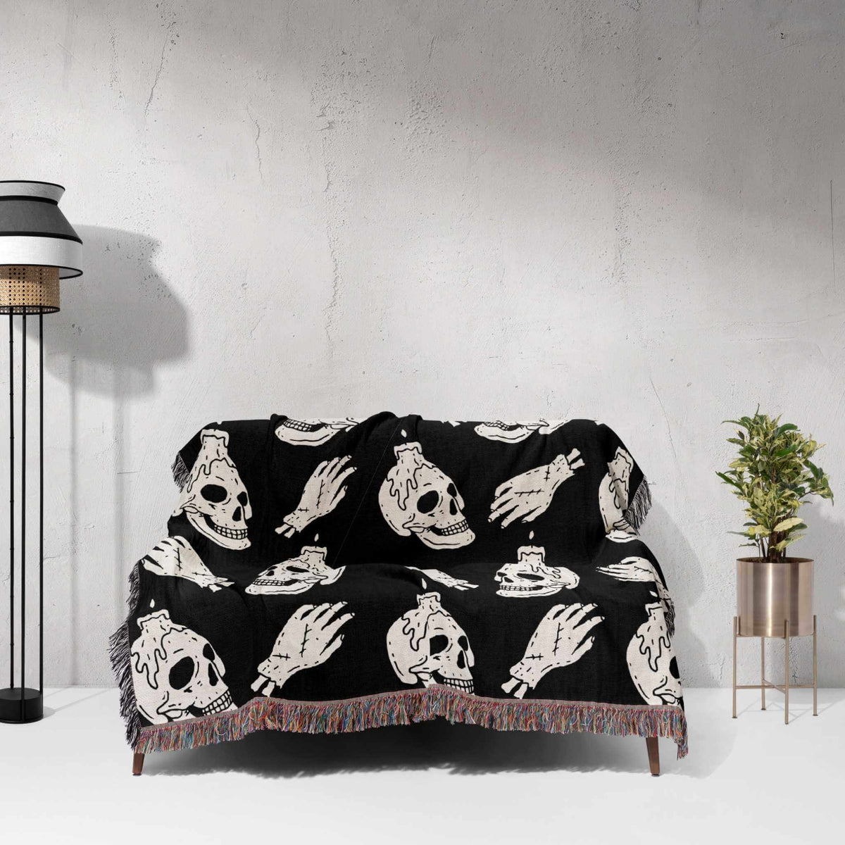 Black blanket with white skull and hand designs draped over a couch against a light gray wall.