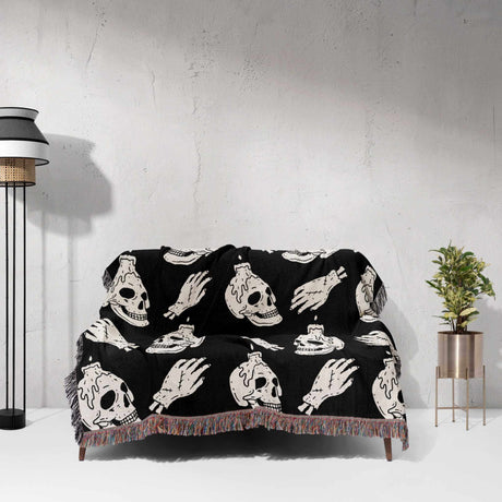 Black blanket with white skull and hand designs draped over a couch against a light gray wall.