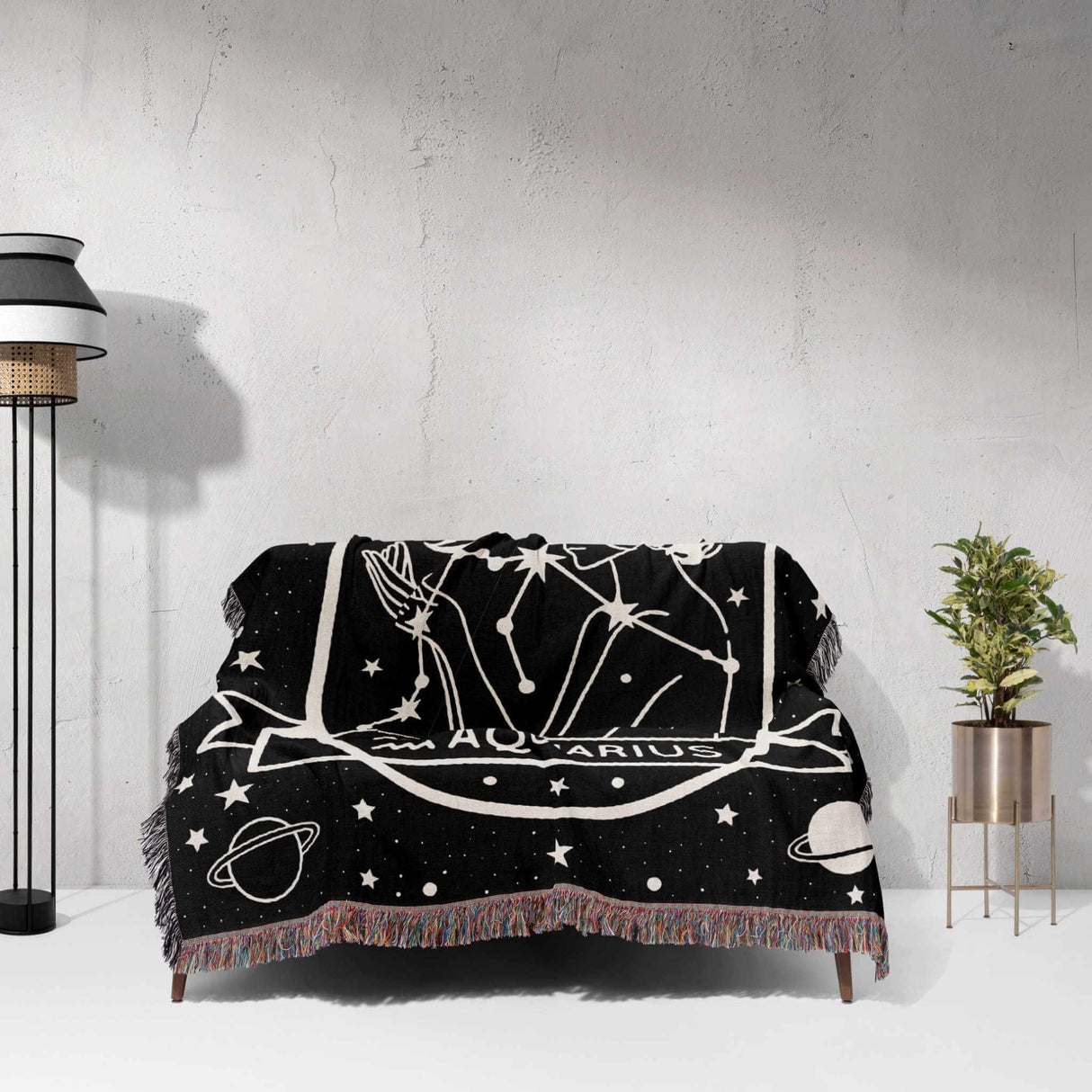 This image shows a Zodiac Sign Blanket draped over a couch, depicting the Aquarius star sign. The woven tapestry blanket features a black-and-white illustration with celestial motifs, enhancing living spaces with astrological charm and comfort.